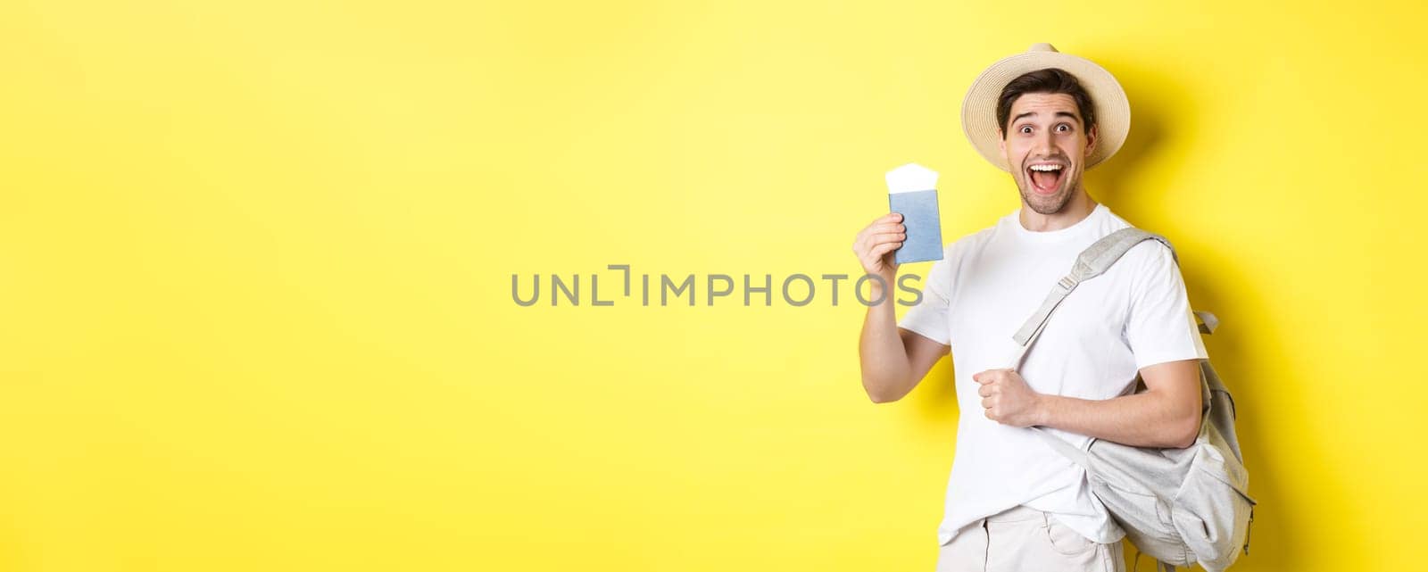 Tourism and vacation. Excited guy tourist going on holiday trip, showing passport with tickets and holding backpack, standing over yellow background.