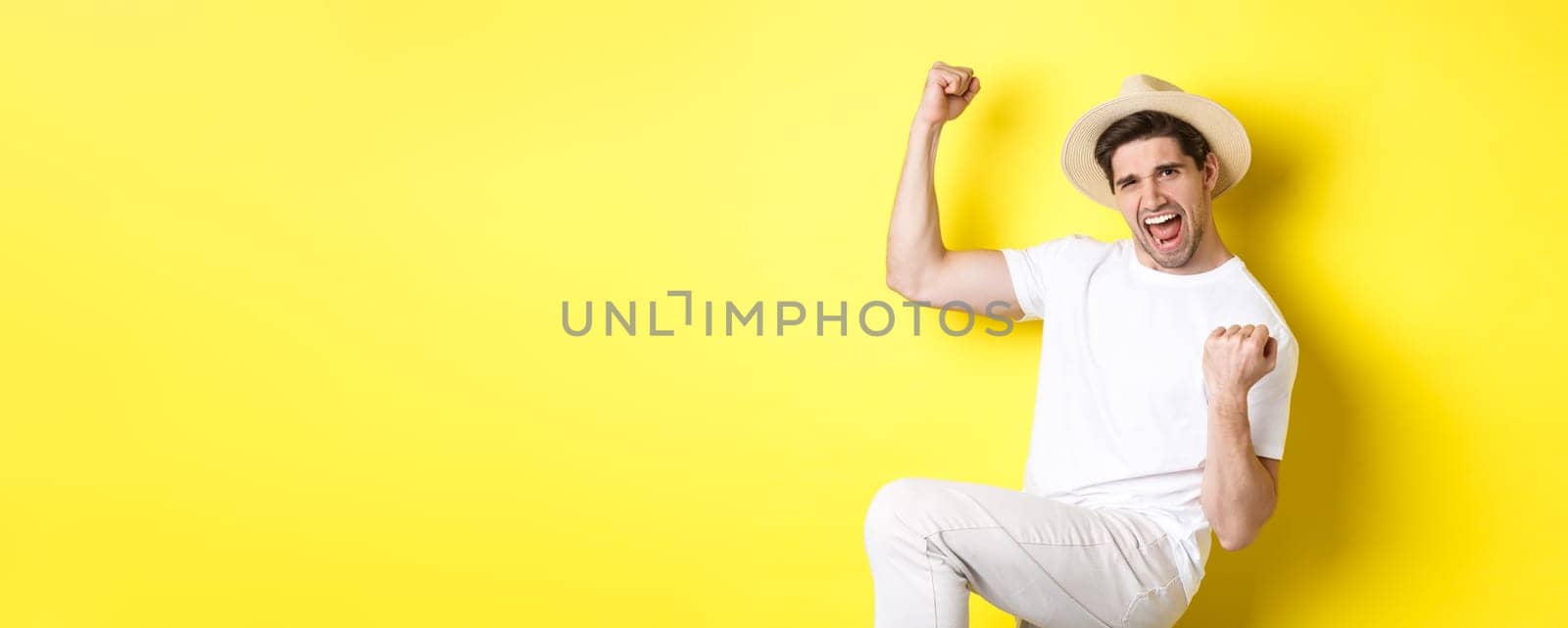 Concept of tourism and vacation. Lucky male tourist winning trip, rejoicing and saying yes, making fist pump while triumphing, standing against yellow background.