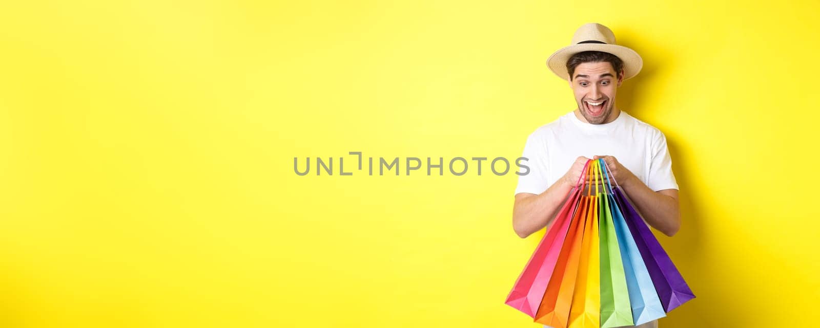 Image of happy man shopping on vacation, holding paper bags and smiling, standing against yellow background by Benzoix