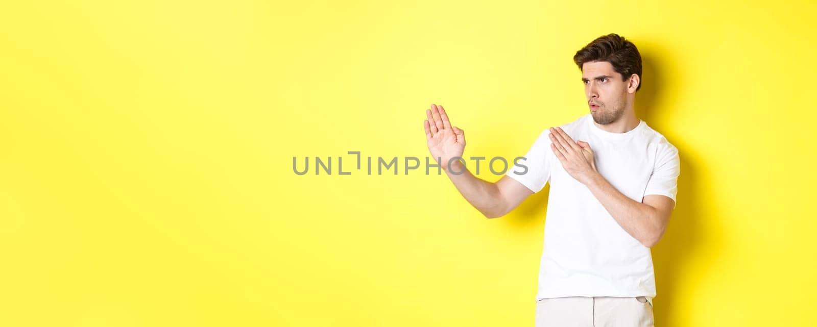 Man showing kung-fu skills, martial arts ninja movement, standing in white t-shirt ready to fight, standing over yellow background.