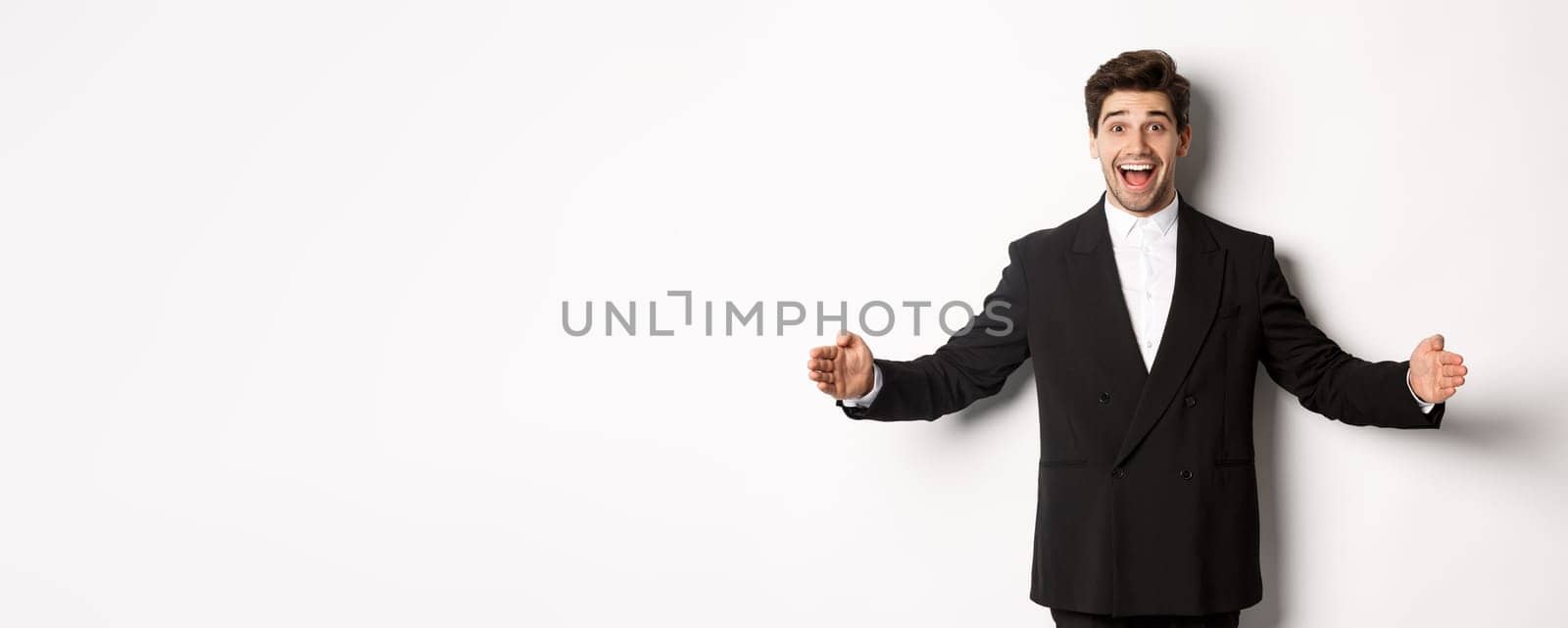 Portrait of excited handsome man in suit, shaping big object on copy space and smiling amazed, holding something, standing over white background by Benzoix