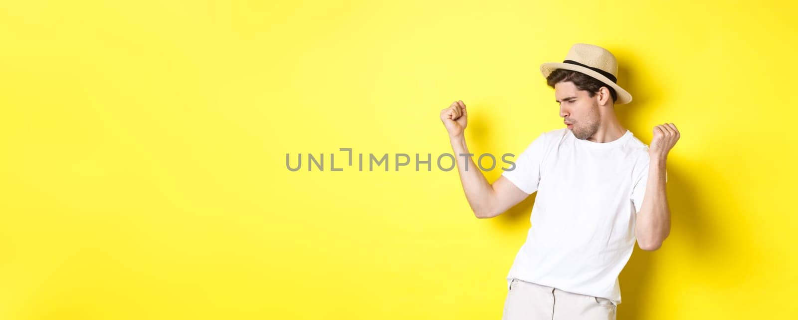 Concept of tourism and vacation. Lucky guy tourist rejoicing, making fist pump and saying yes, standing pleased against yellow background.