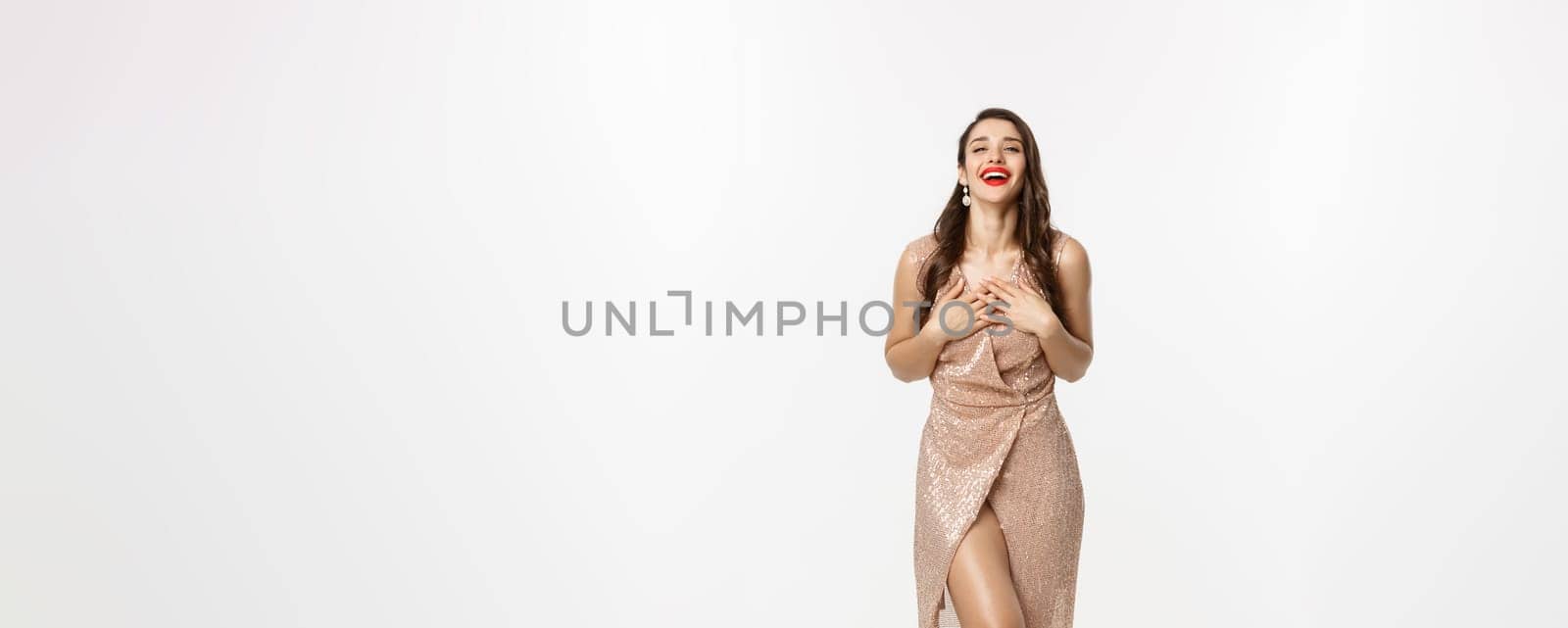 Christmas party and celebration concept. Glamour woman in elegant dress, looking touched and thankful, laughing coquettish, white background.