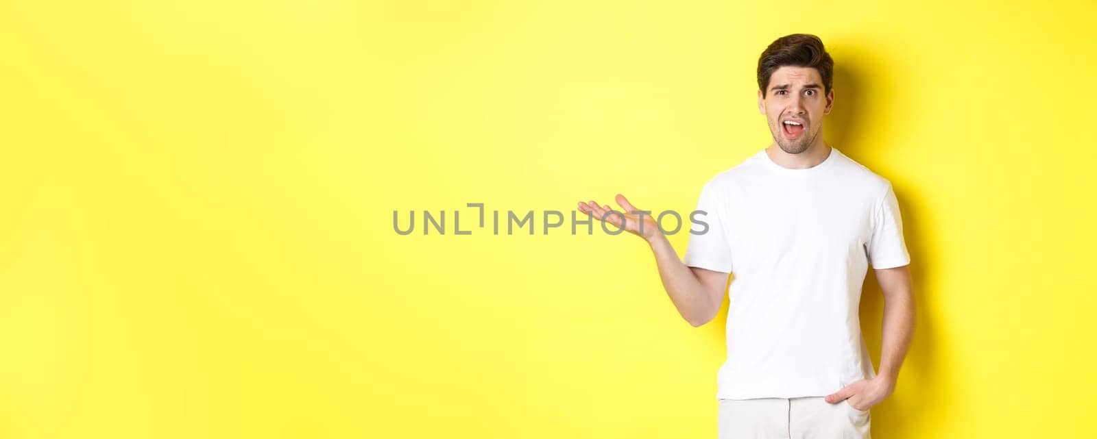 Confused and shocked man complaining, raising one hand and looking bothered, standing near yellow copy space by Benzoix