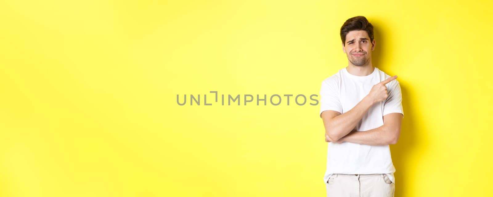 Skeptical and unamused man pointing finger right at something lame, frowning reluctant, standing over yellow background by Benzoix