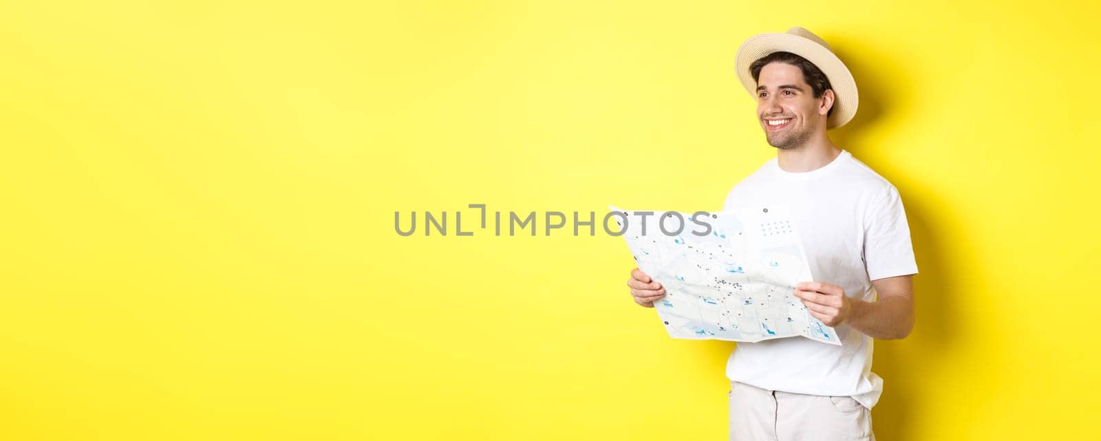 Travelling, vacation and tourism concept. Handsome guy tourist going sightseeing, holding map and smiling, standing over yellow background.