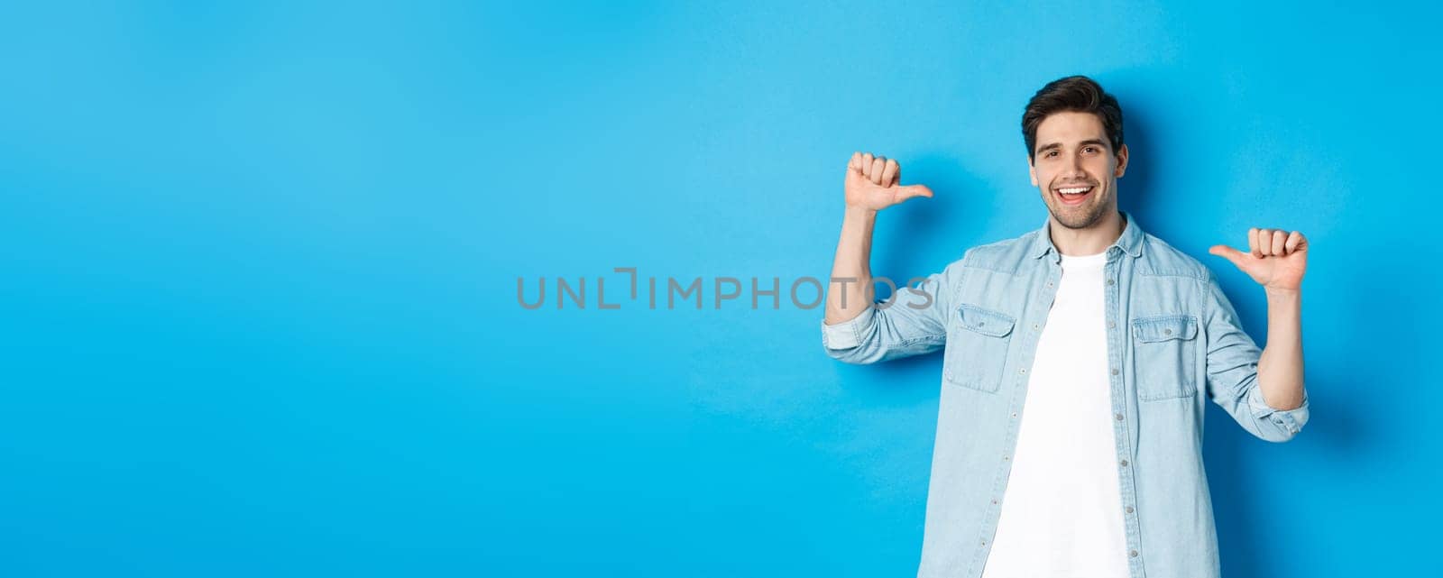 Portrait of confident man pointing at himself, being a professional, bragging while standing against blue background by Benzoix