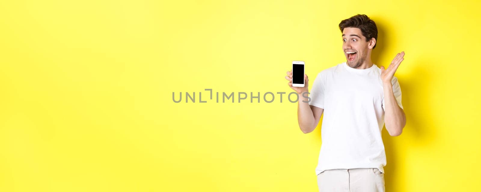 Image of amazed guy looking at mobile phone screen with surprised face, standing excited against yellow background by Benzoix