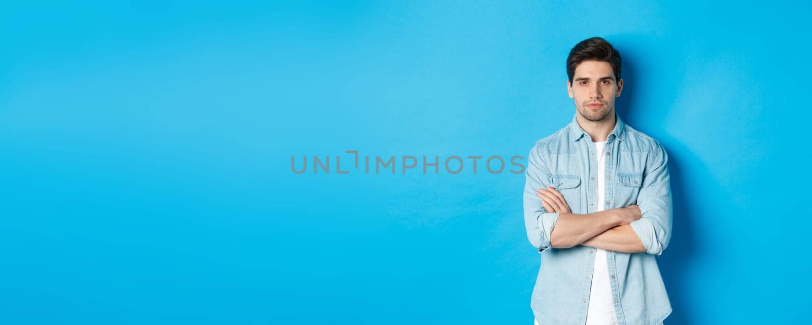 Image of handsome caucasian man in casual outfit, looking serious and confident, standing against blue background by Benzoix