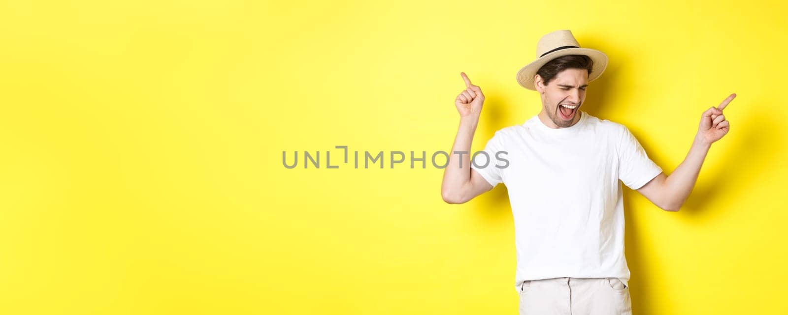 Concept of tourism and lifestyle. Happy man enjoying vacation, tourist dancing over yellow background.