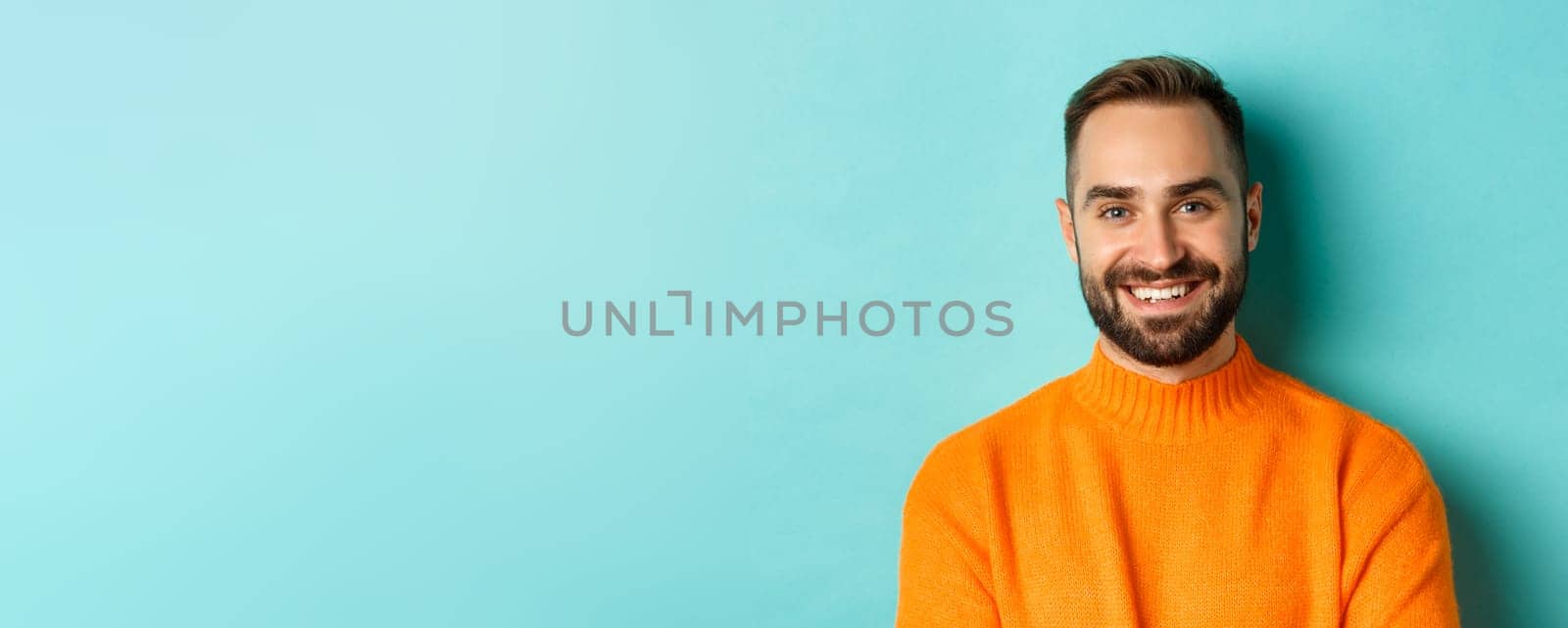 Close-up of handsome caucasian man smiling at camera, looking confident, wearing orange sweater, standing against turquoise background by Benzoix