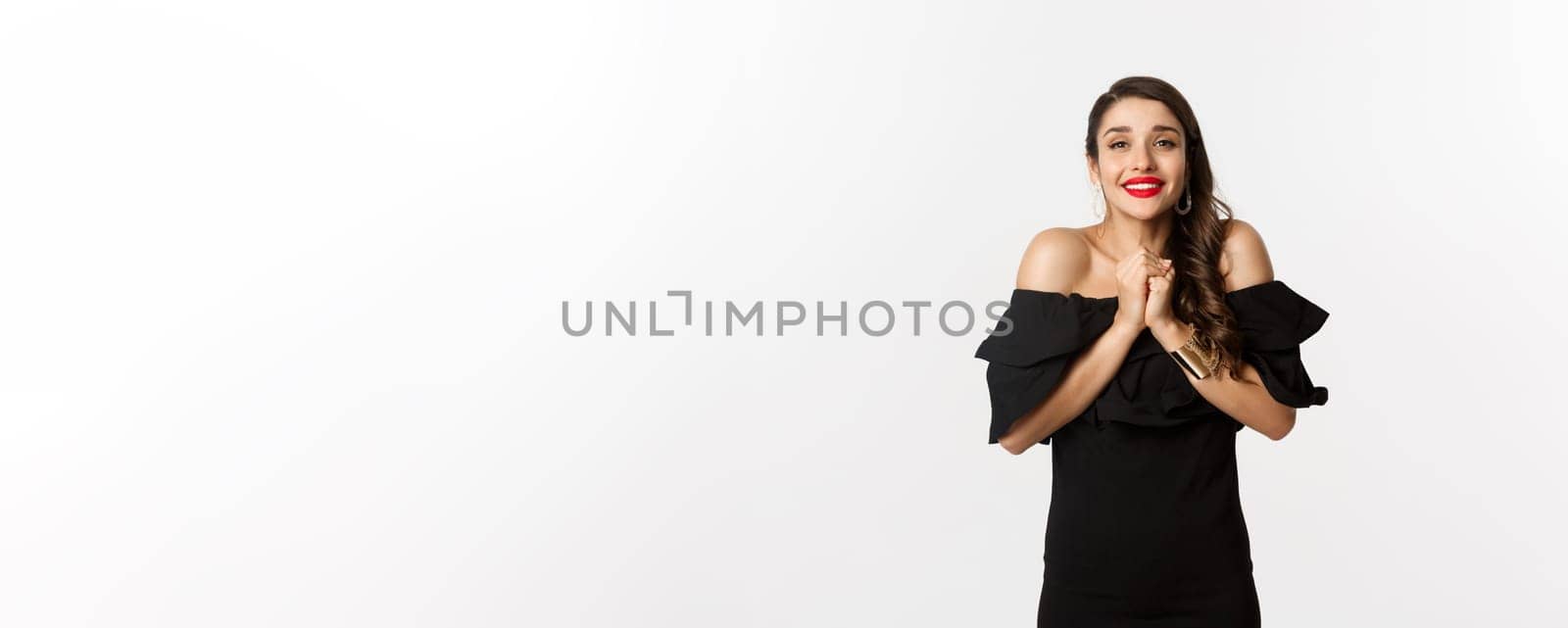 Fashion and beauty. Pretty woman in black dress asking for help, showing thank you gesture, looking grateful at camera, standing over white background by Benzoix