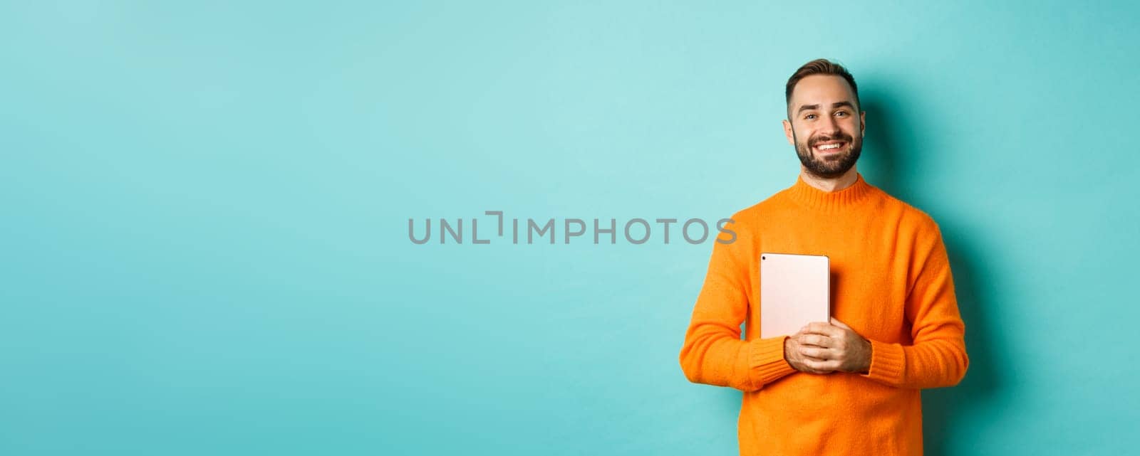 Handsome freelancer man holding laptop and smiling, standing happy over light blue background.