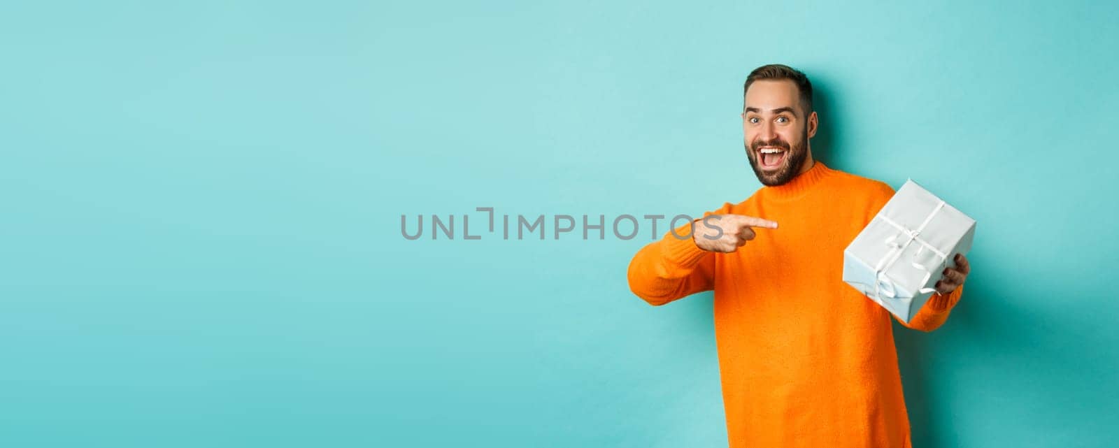 Holidays and celebration concept. Excited man receiving gift, looking happy at present and smiling, standing over blue background by Benzoix