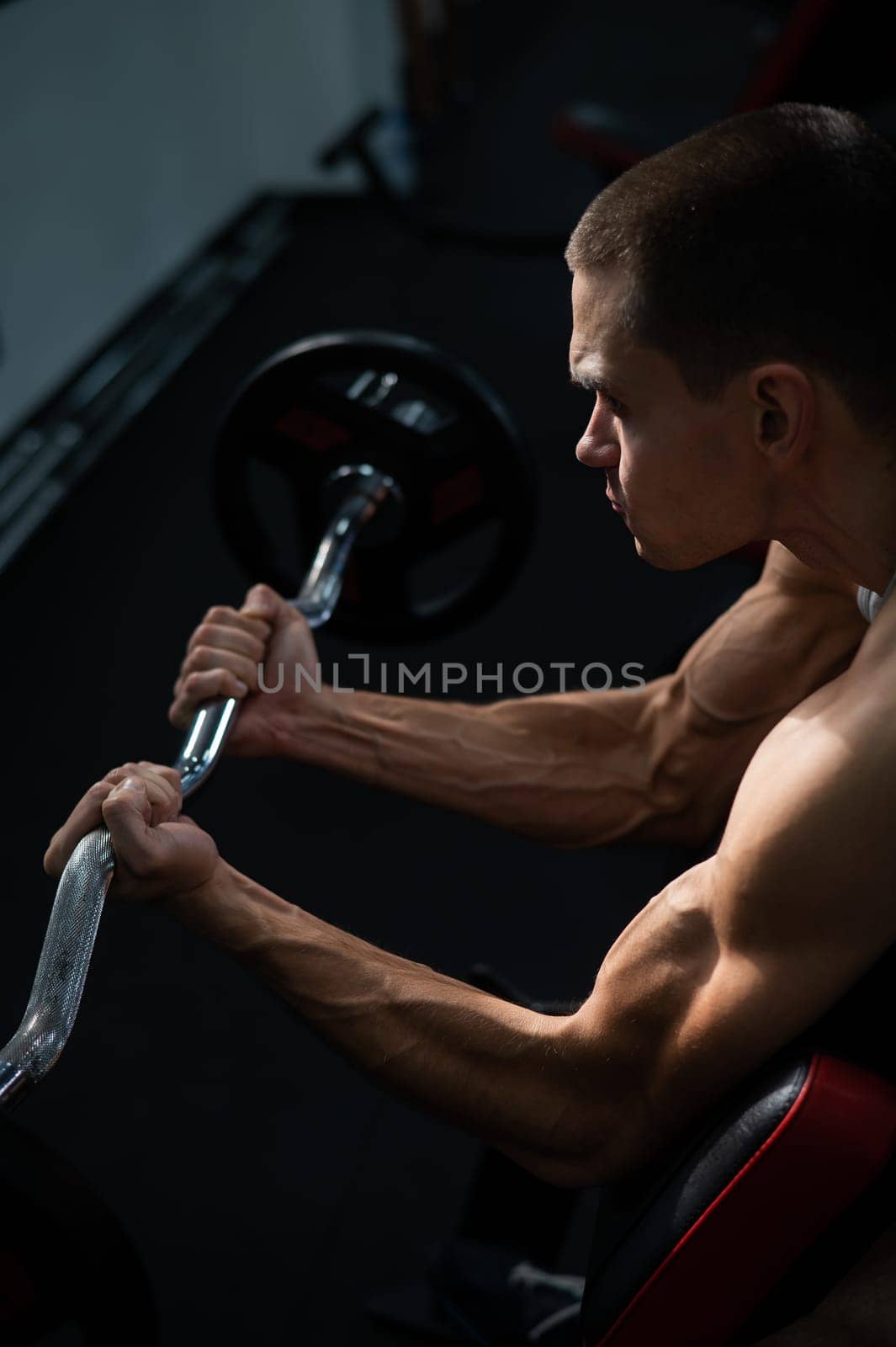 Man doing EZ barbell bicep exercises on Scott bench