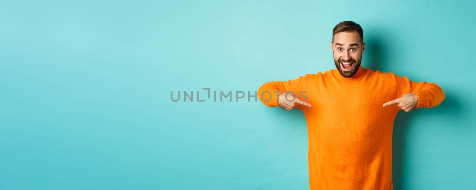 Happy man pointing at sweater, showing your logo banner on clothes, standing over light blue background.