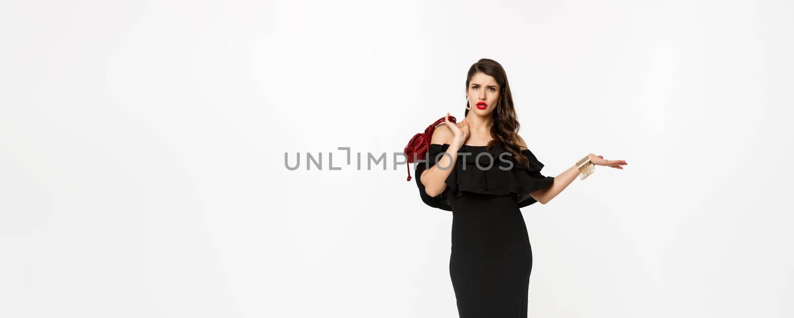 Beauty and fashion concept. Full length of arrogant and sassy woman in black dress, holding purse on shoulder and stroll forward at camera, posing over white background.