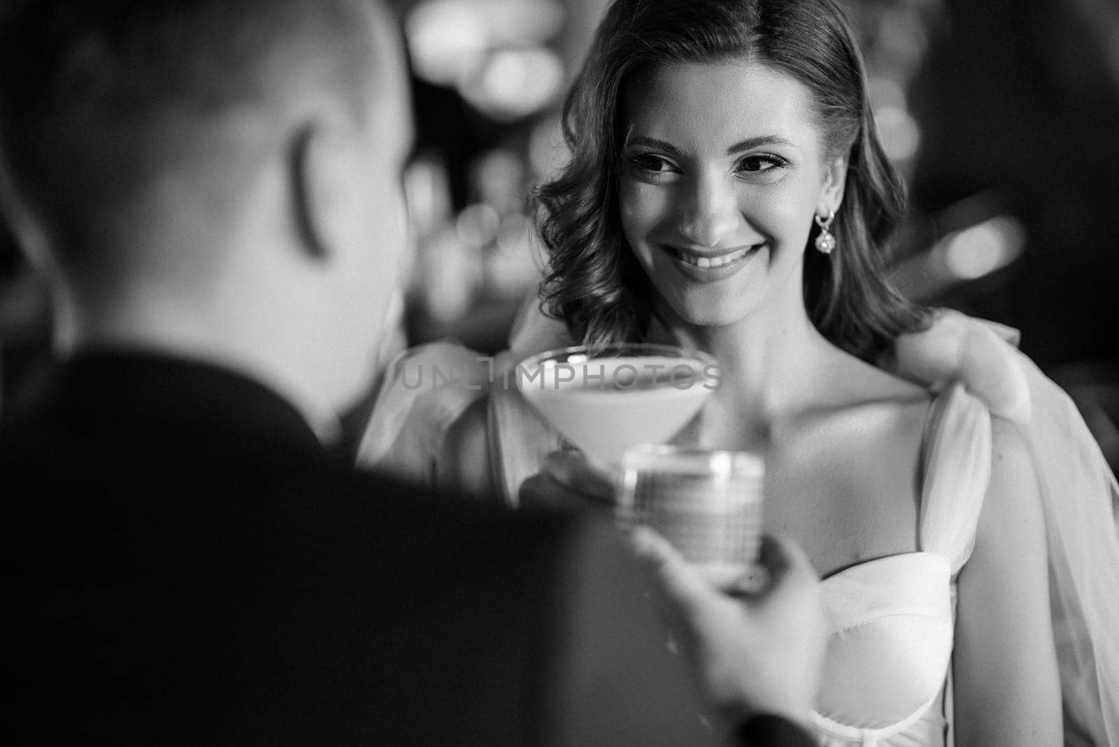 bride and groom inside a cocktail bar in a bright atmosphere with a glass of drink
