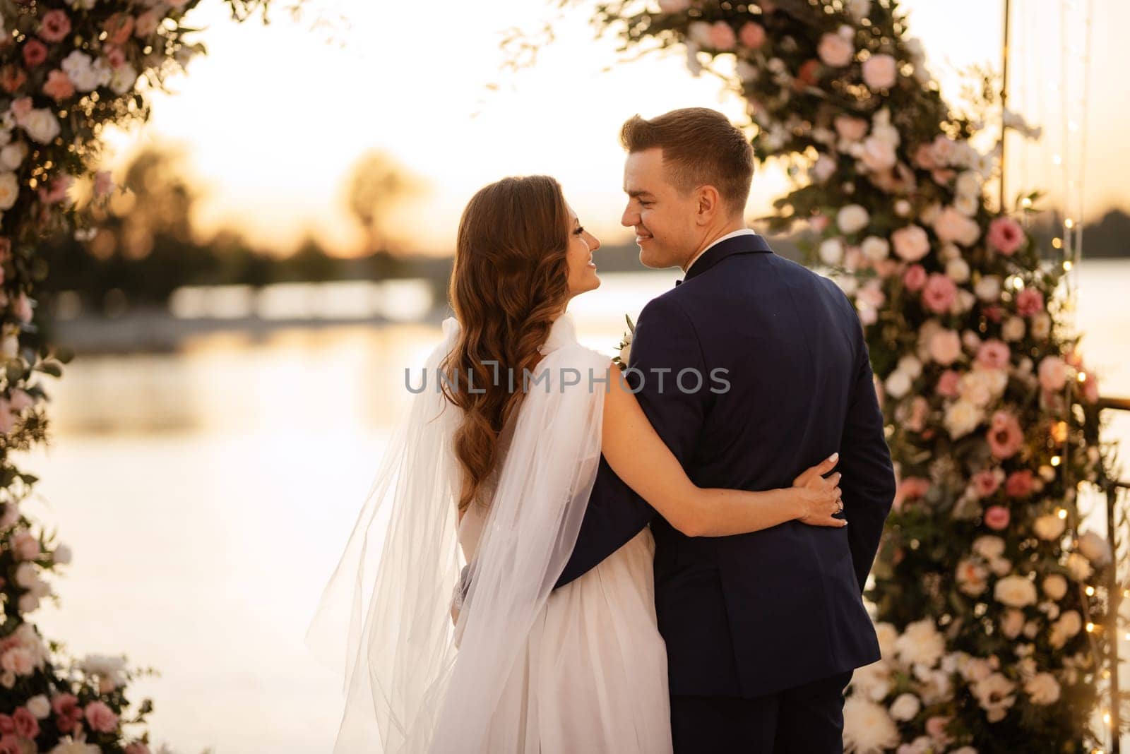 bride and groom against the backdrop of a yellow sunset on a pier near the river