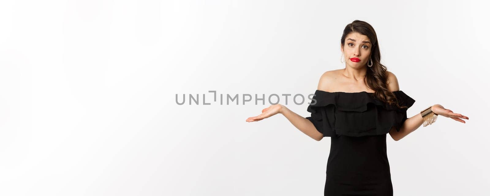 Fashion and beauty. Clueless attractive woman in black dress dont know, shrugging and smirking unaware, standing indecisive over white background.