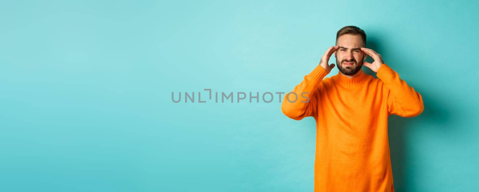 Photo of caucasian man touching head, feeling sick, have headache or migraine, hangover after party, standing over light blue background by Benzoix