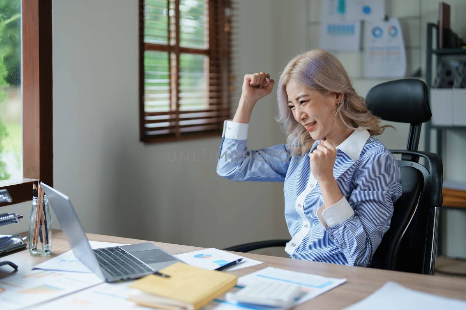 Portrait of a woman business owner showing a happy smiling face as he has successfully invested her business using computers and financial budget documents at work.