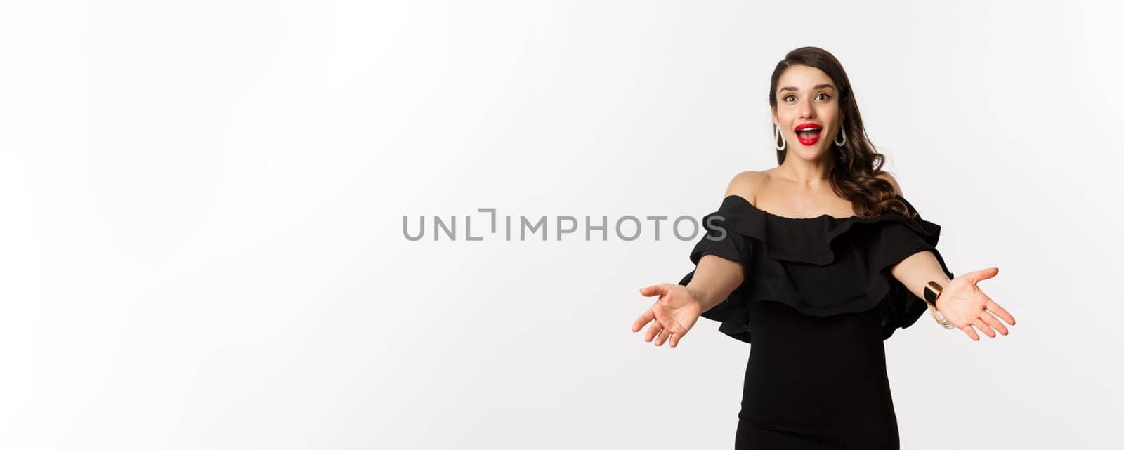 Fashion and beauty concept. Happy young woman in glamour black dress, reaching hands forward to take something, waiting for hug, white background.