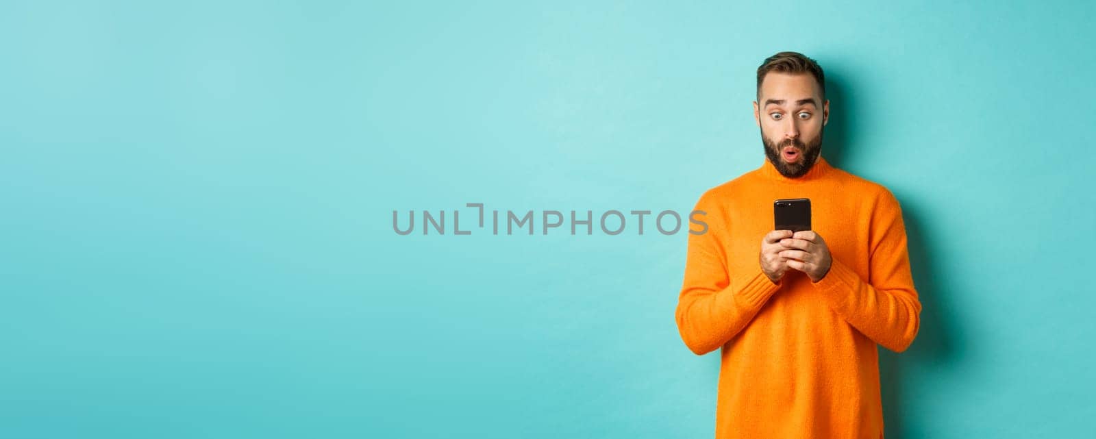 Image of man reading message with surprised face, standing amazed over light blue background.