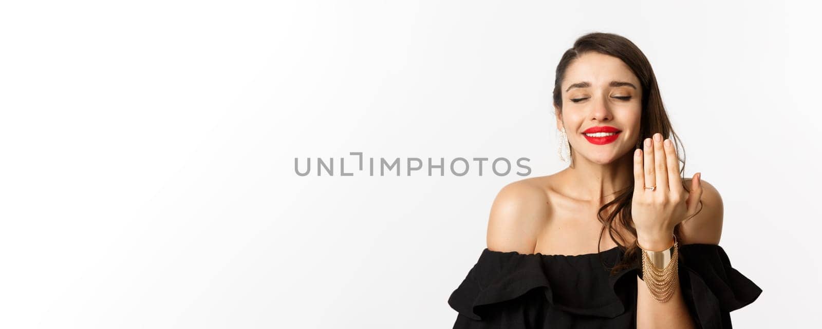 Happy young woman saying yes, become a bride, showing engagement ring on finger and smiling pleased, standing over white background by Benzoix