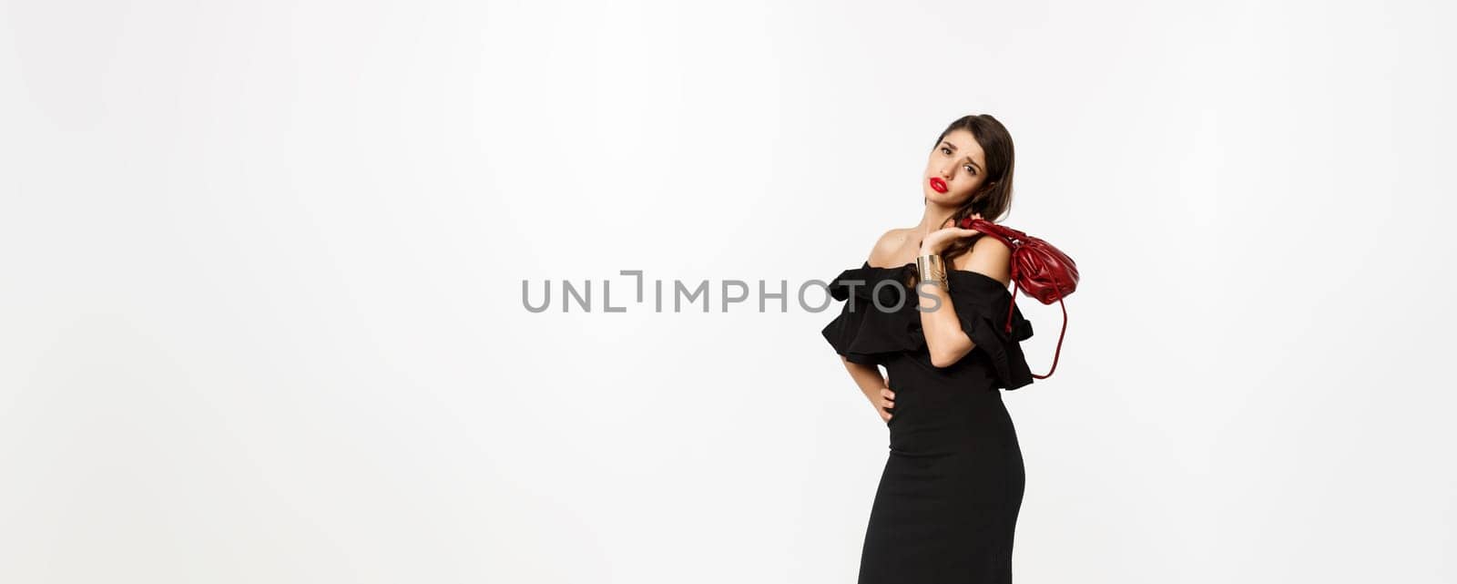 Beauty and fashion concept. Full length of tired young woman in high heels and elegant dress, holding purse on shoulder and looking with fatigue at camera, white background by Benzoix