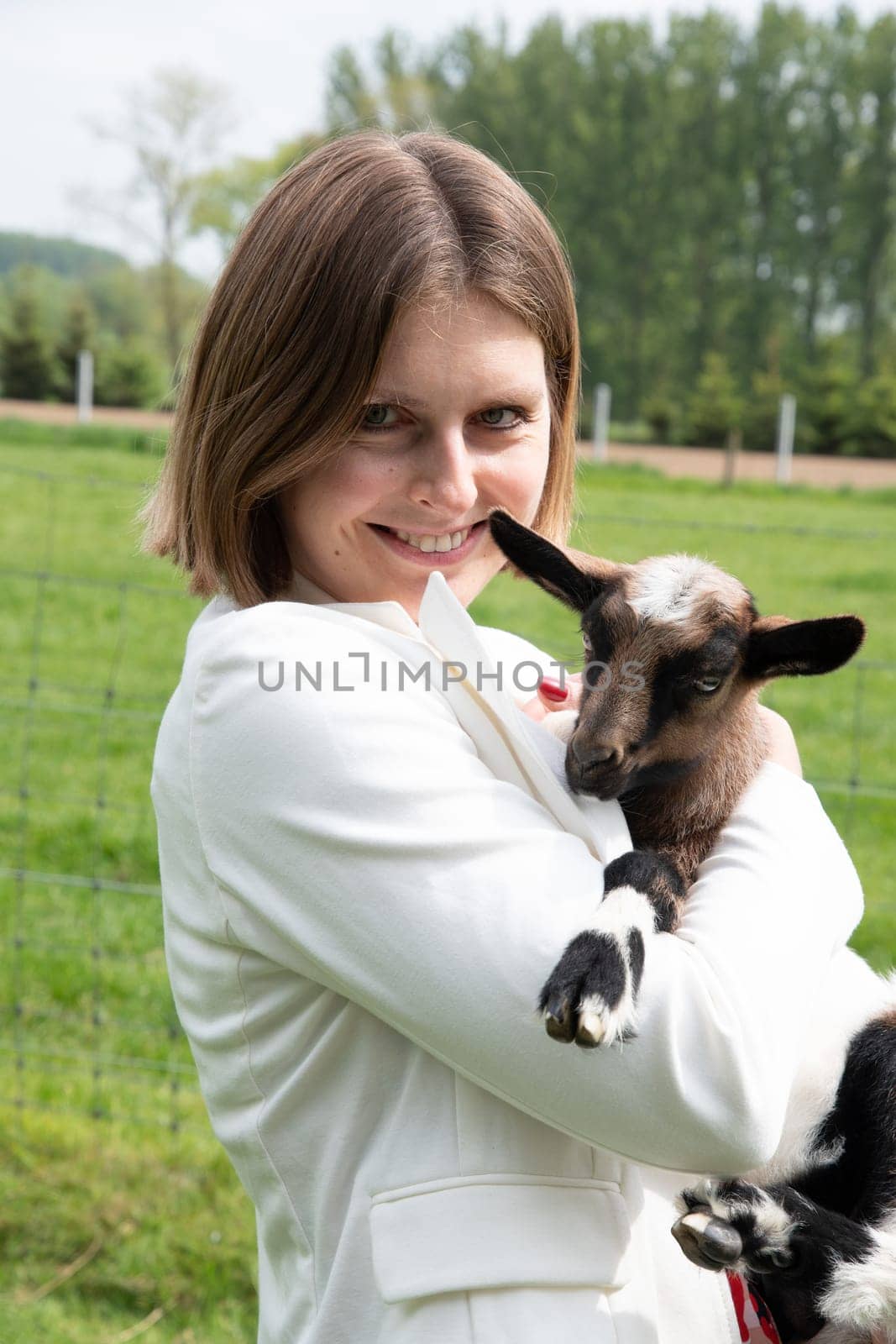 Young woman plays with goat kids, feeding them, sun shining over farm in background, High quality photo