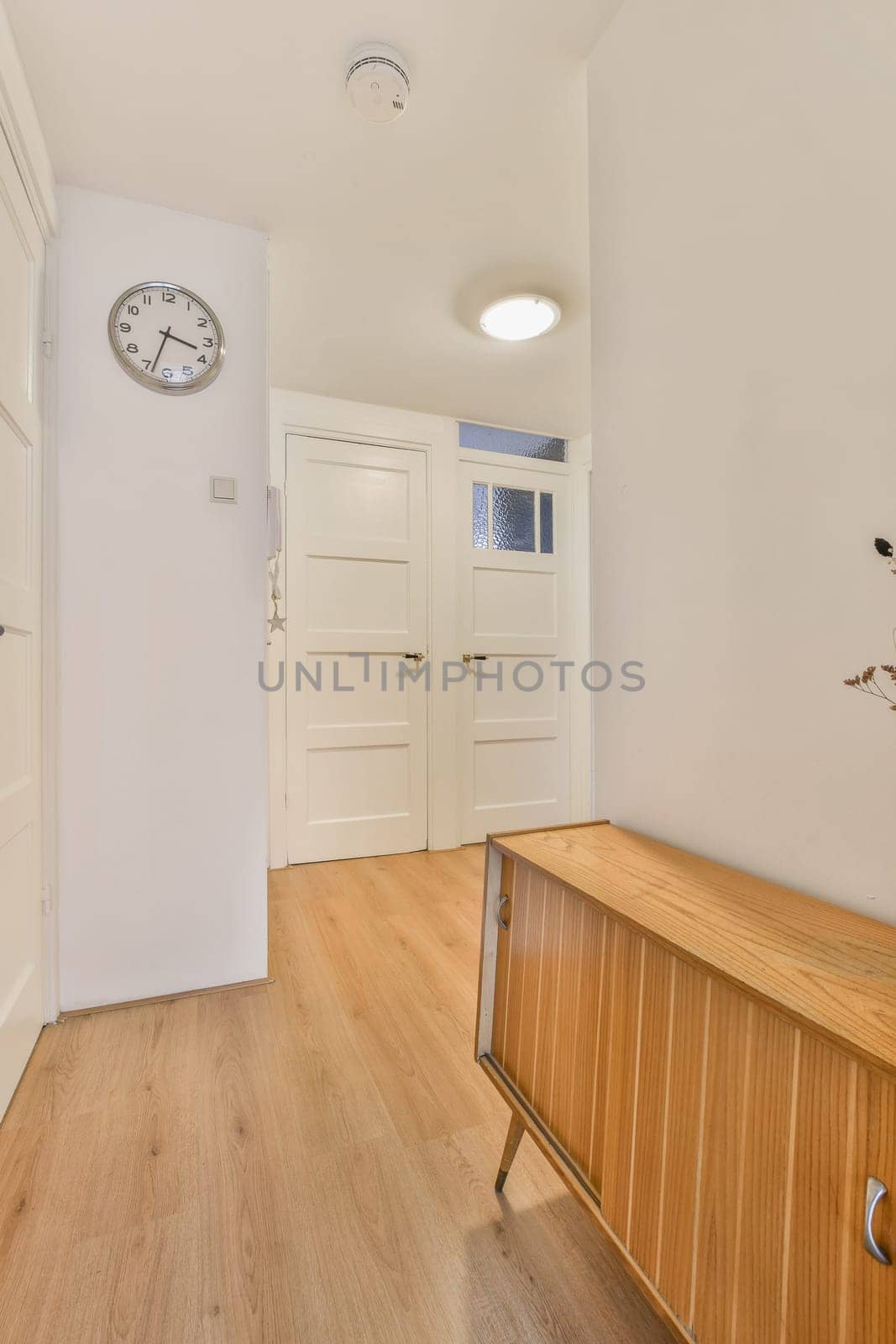 an empty room with a clock on the wall and hardwood flooring in front of the door to the other room