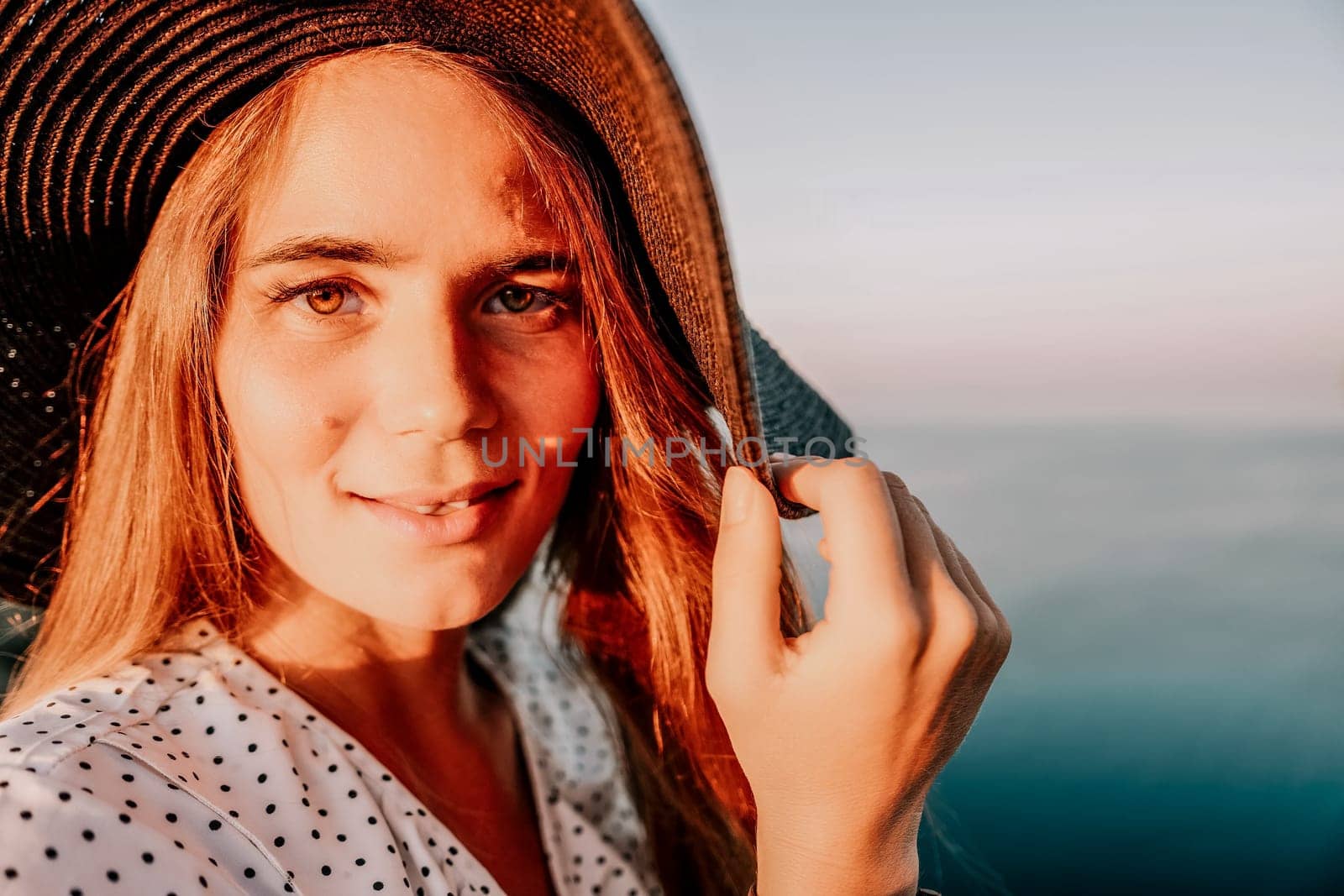 Portrait of happy young woman wearing summer black hat with large brim at beach on sunset. Closeup face of attractive girl with black straw hat. Happy young woman smiling and looking at camera at sea. by panophotograph