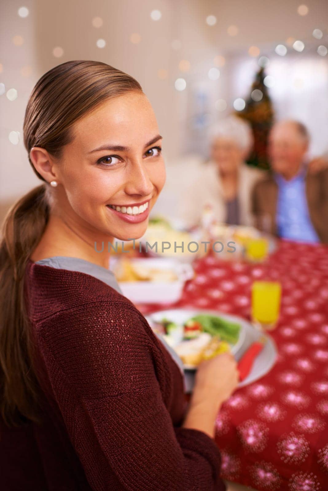 Good food and great family moments. A young woman smiling at the christmas table with her family in the background