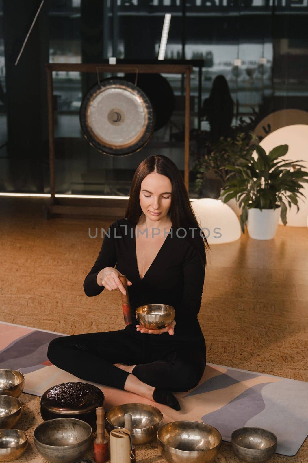 A woman in the lotus position using a singing bowl indoors . Relaxation and meditation. Sound therapy, alternative medicine. Buddhist healing practices by Lobachad