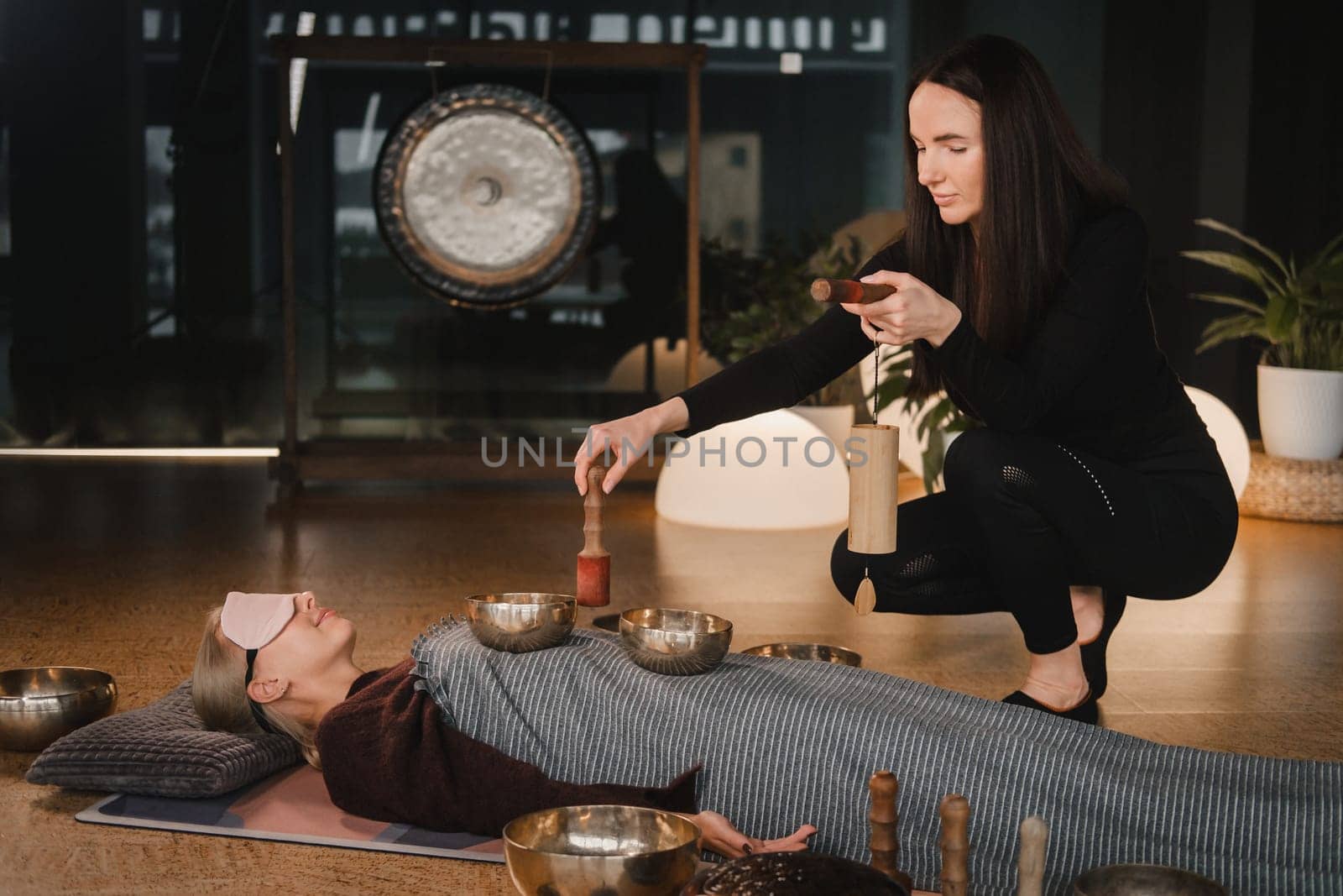 A young beautiful woman is doing a massage with singing bowls and a koshi bell to another girl. Sound therapy by Lobachad