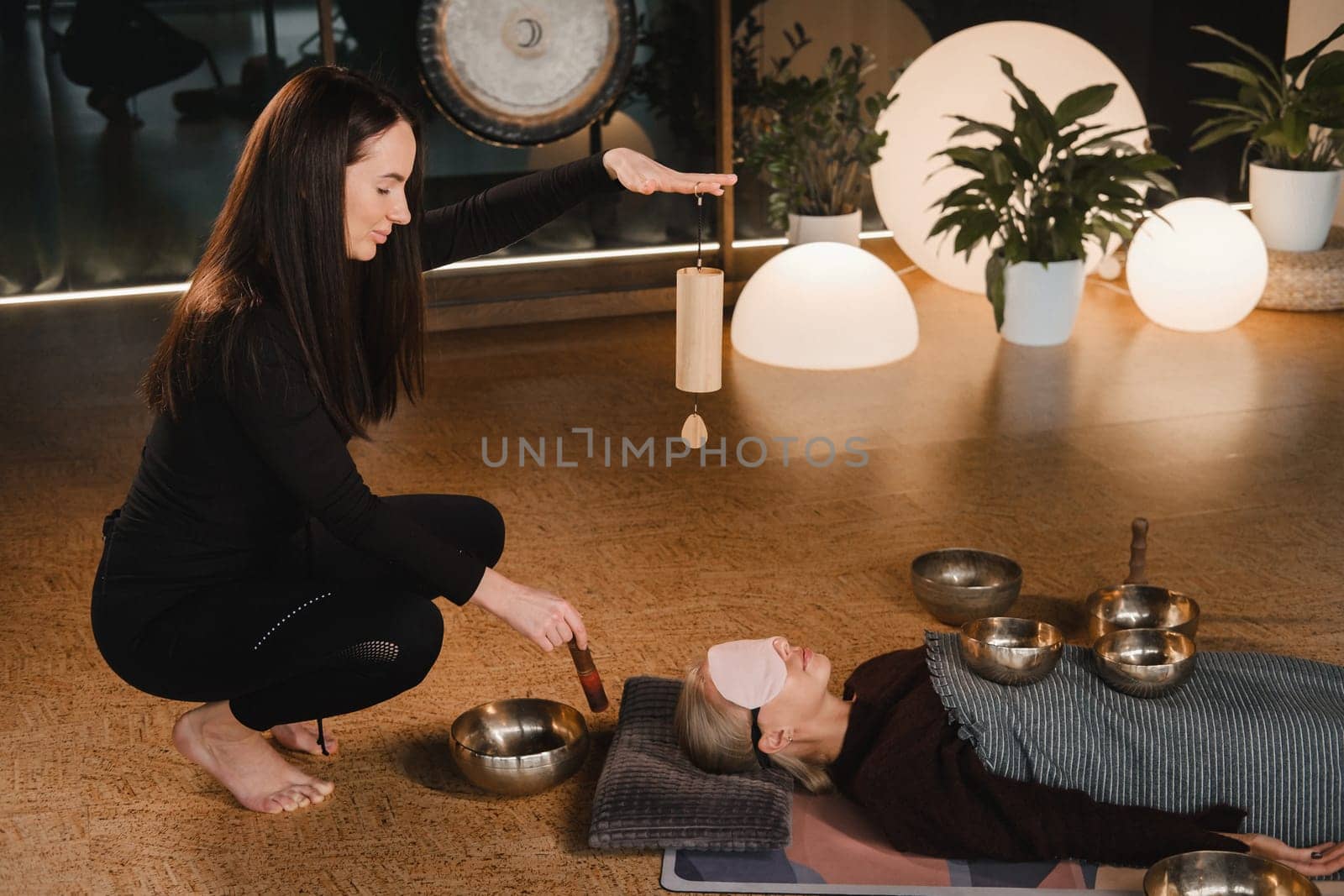 A young beautiful woman is doing a massage with singing bowls and a koshi bell to another girl. Sound therapy by Lobachad
