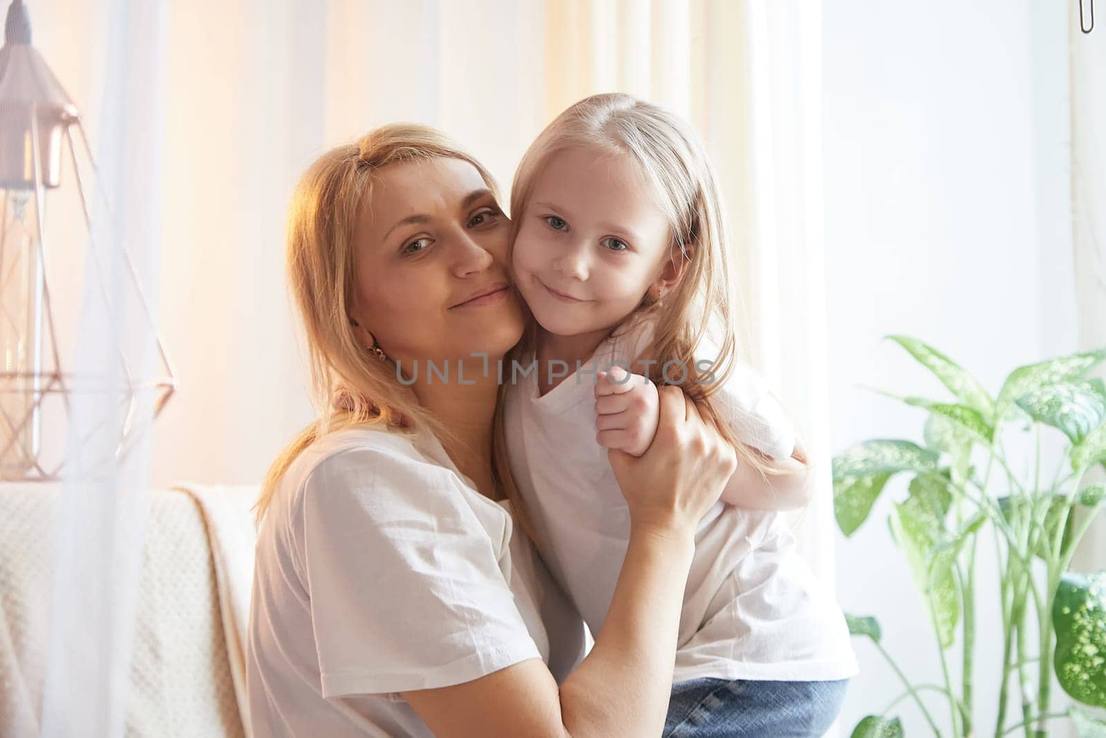 Happy loving family with mother and daughter having hugs in living room. Woman mom and small child girl inside of home