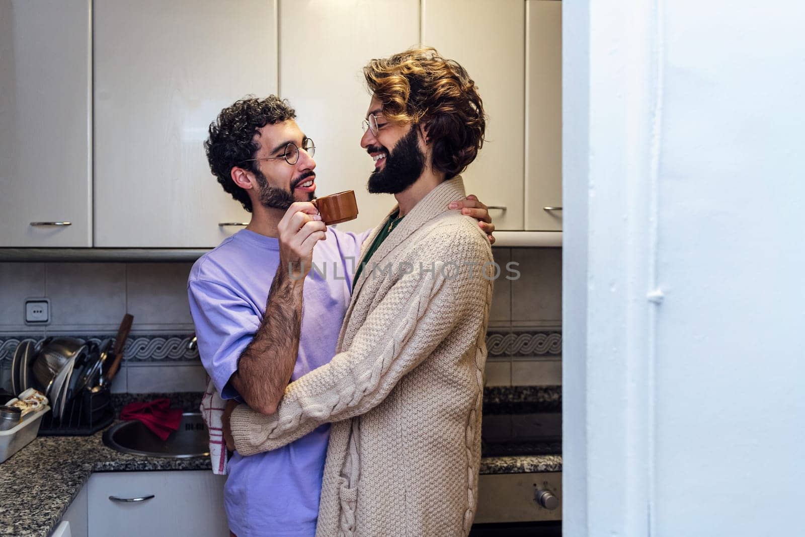 gay male couple hugging affectionately while having morning coffee in the kitchen, concept of home lifestyle and love between people of the same sex, copy space for text