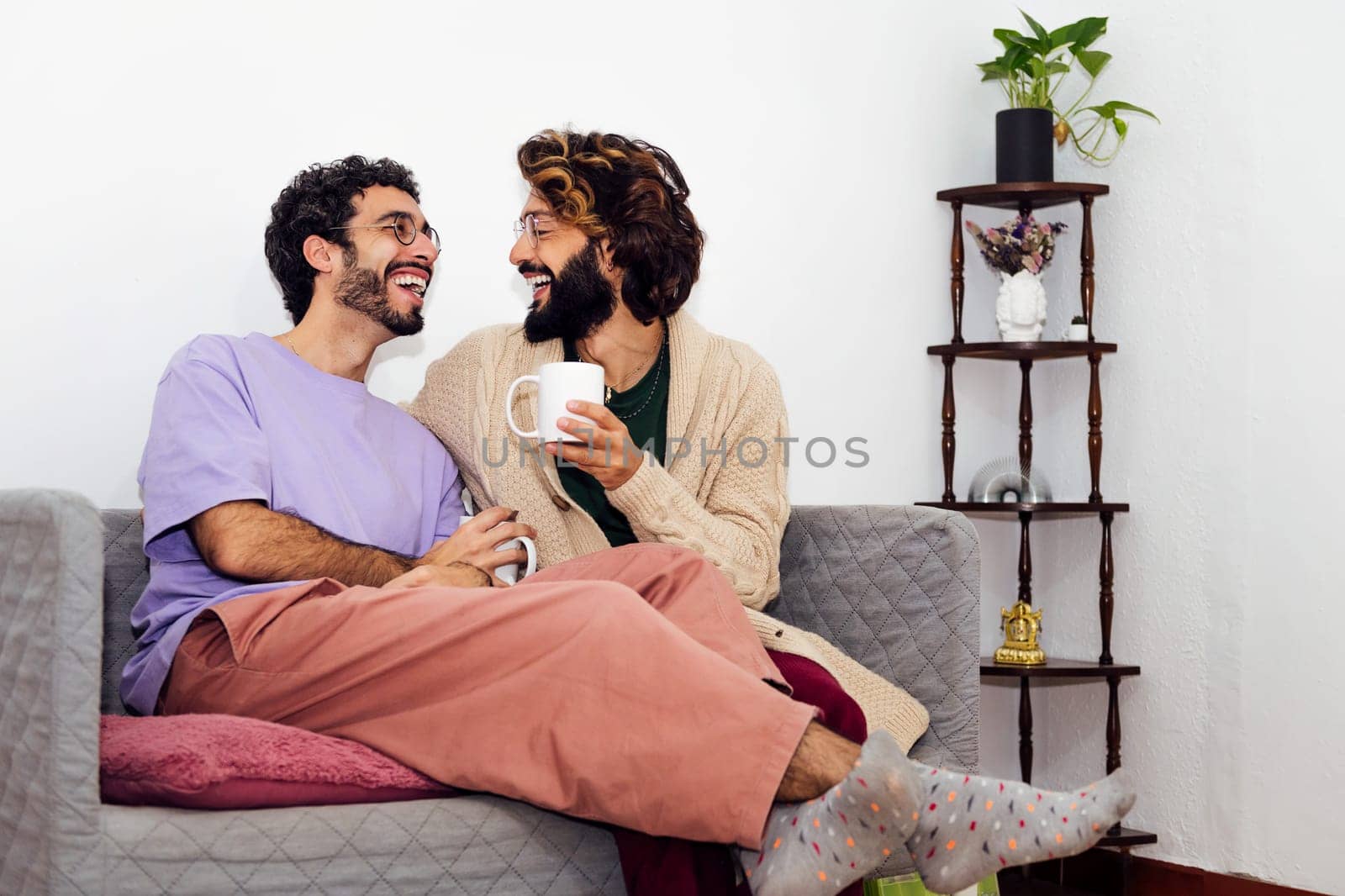 gay male couple laughing relaxed on the couch at home, concept of real people lifestyle at home, copy space for text
