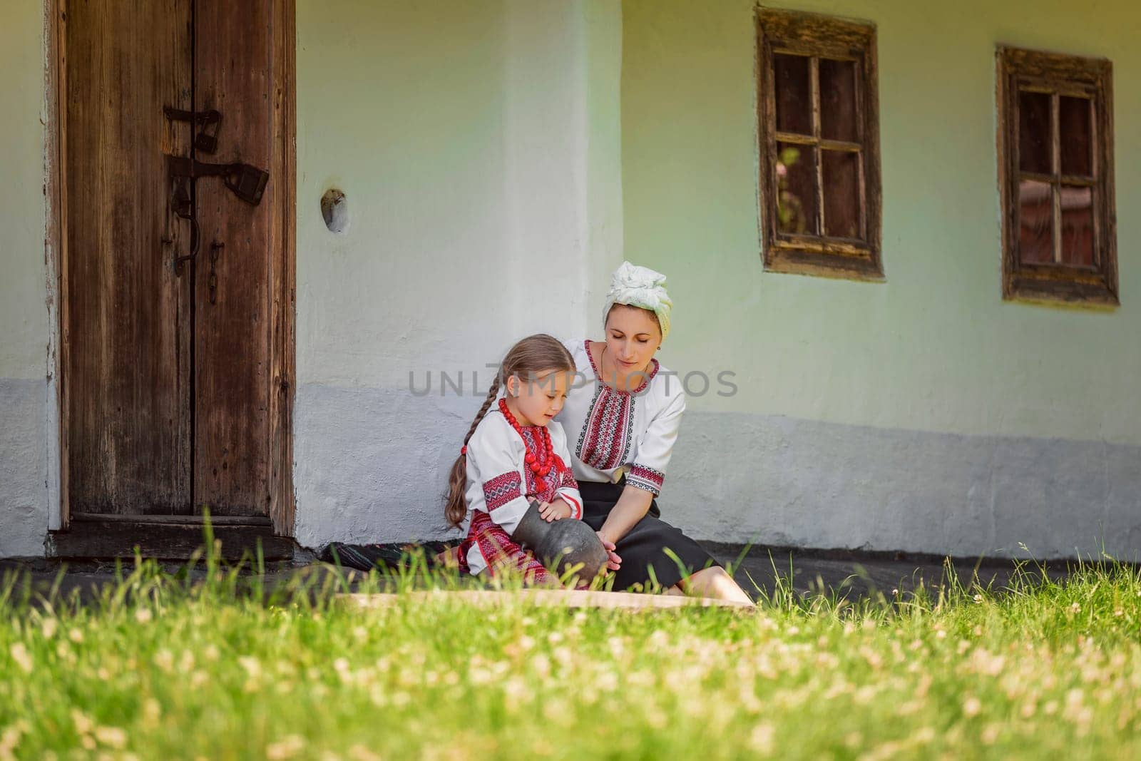 mother and daughter in traditional Ukrainian clothes are sitting near the house