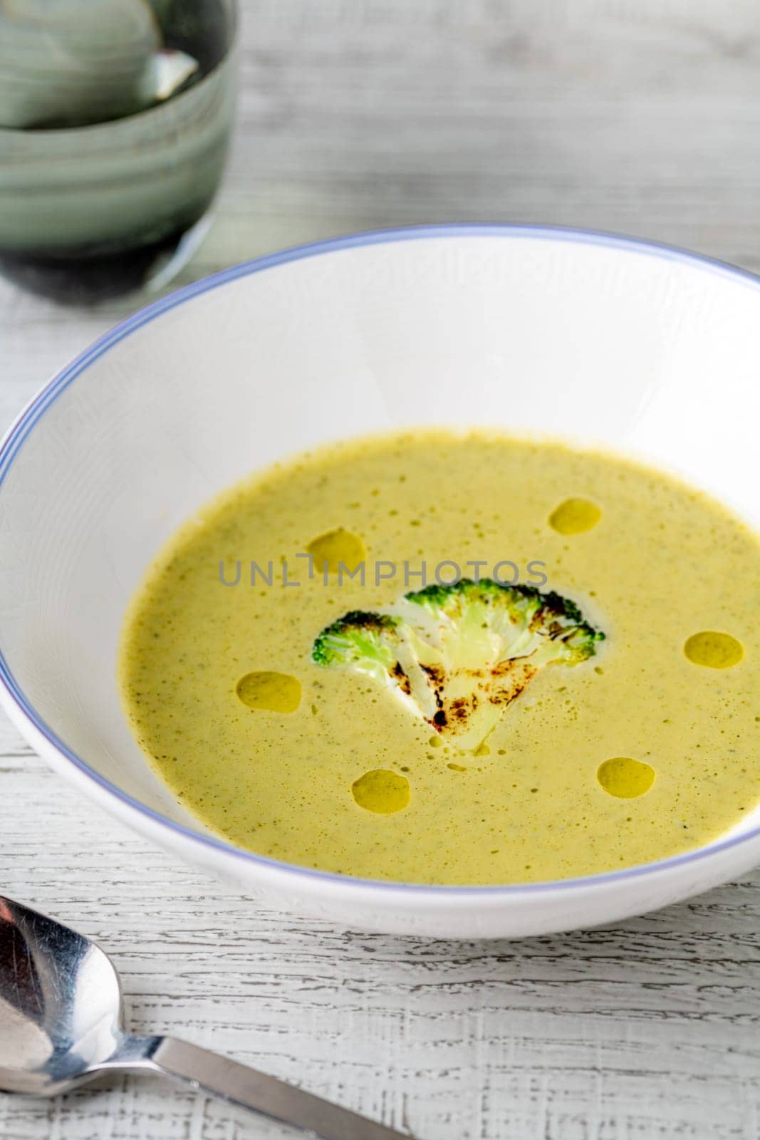 Healthy broccoli soup with a slice of grilled broccoli on a white porcelain plate by Sonat