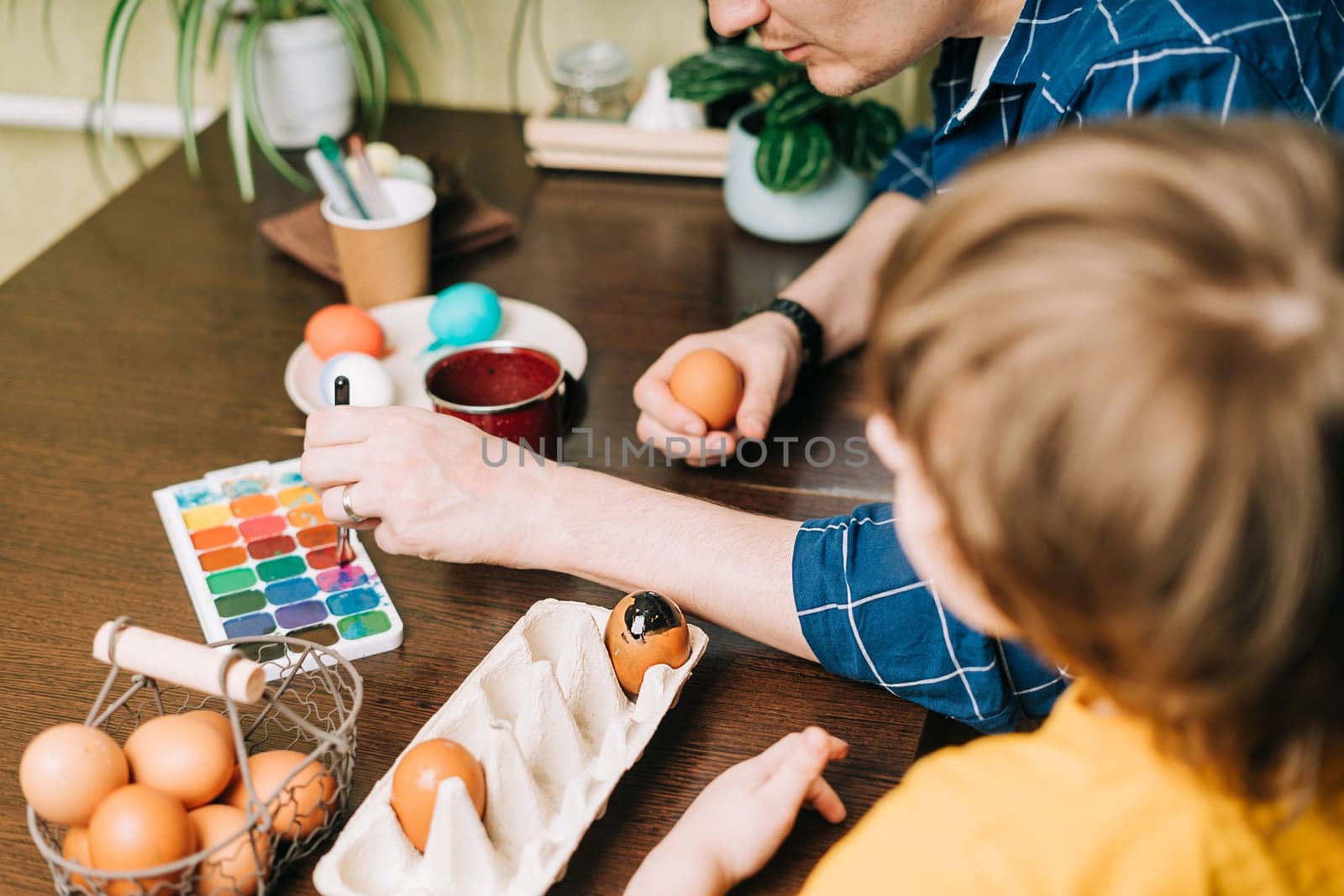 Easter day. Male Father and son painting eggs on wooden background. Family sitting in a kitchen. Preparing for Easter, creative homemade decoration. Child kid boy having fun and painting easter eggs