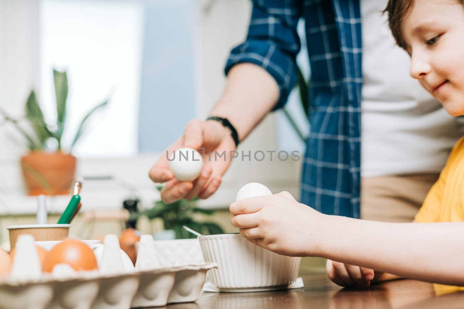 Easter day. Male Father and son painting eggs on wooden background. Family sitting in a kitchen. Preparing for Easter, creative homemade decoration. Child kid boy having fun and painting easter eggs