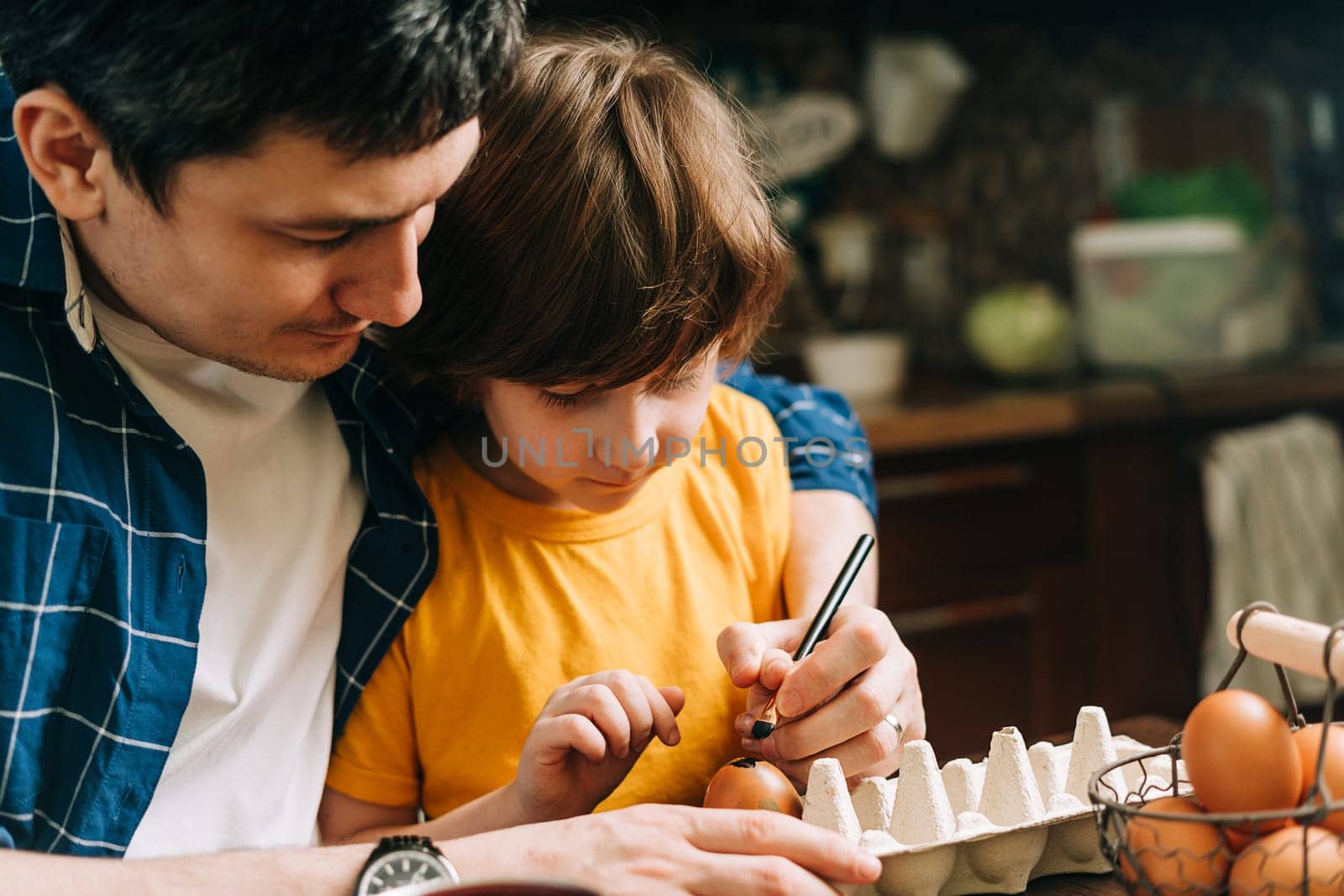 Easter day. Male Father and son painting eggs on wooden background. Family sitting in a kitchen. Preparing for Easter, creative homemade decoration. Child kid boy having fun and painting easter eggs