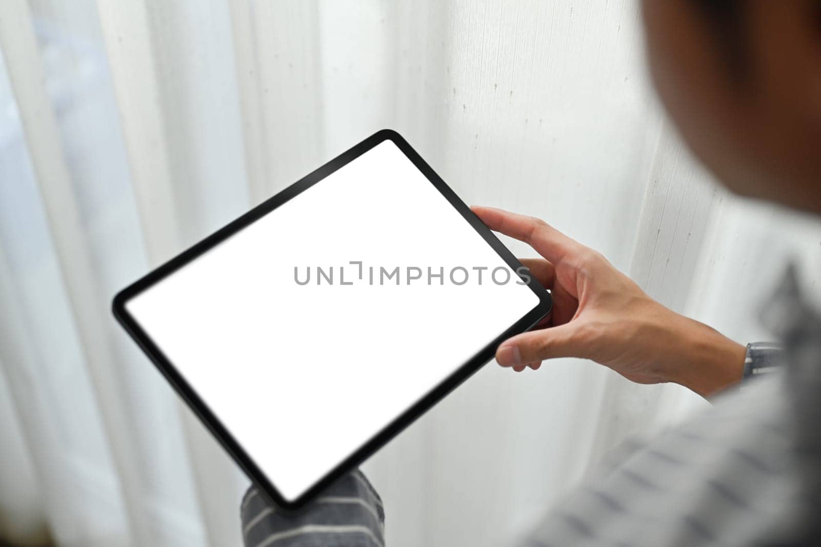 Close up view of man hand holding holding digital tablet while sitting in living room. White screen for webpage or advertise text.