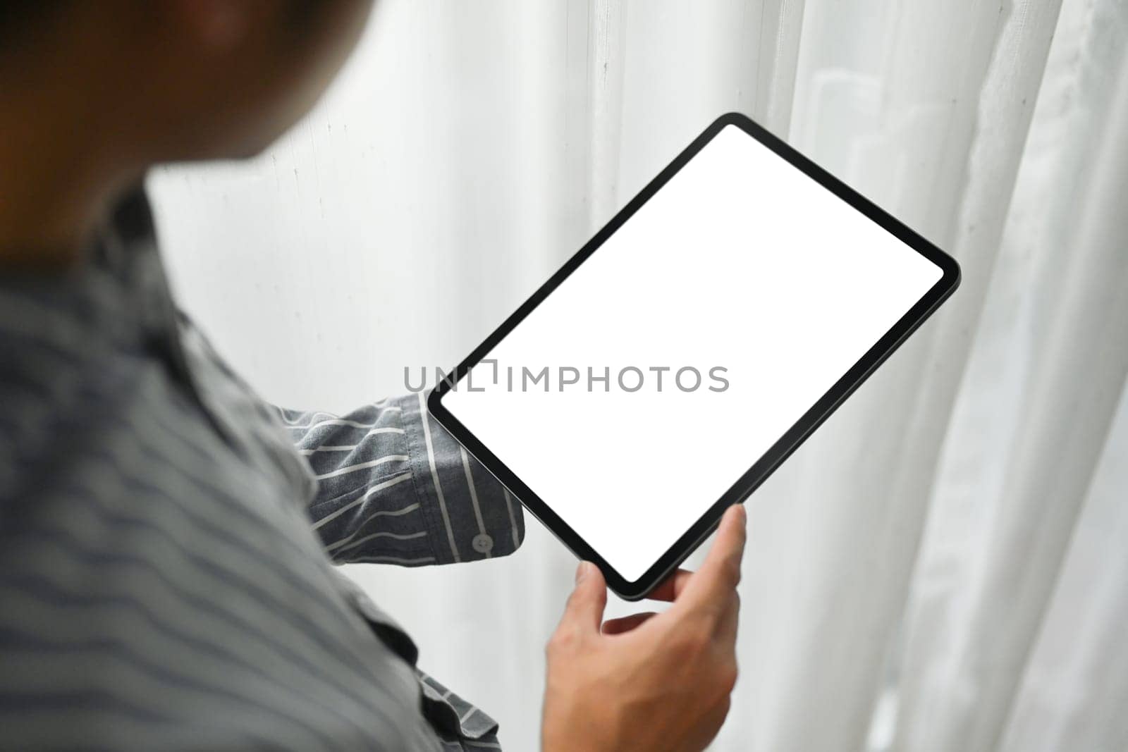 Over shoulder view of businessman hands holding digital tablet. White empty screen and blank space for your text.