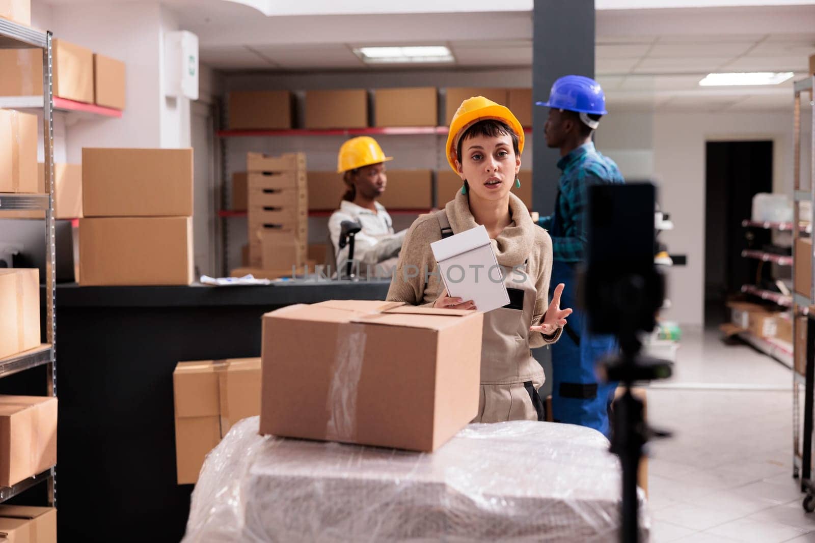 Retail storehouse worker recording smartphone video with goods unpacking. Young warehouse employee explaining stock supply management and order packing on mobile phone camera