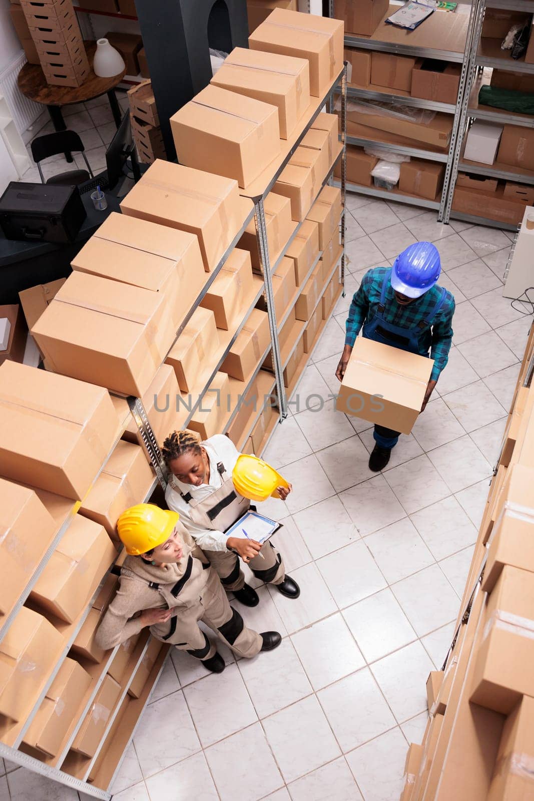 Post office storage operators managing parcel transportation. Storehouse workers standing with customer orders list near shelf full of cardboard boxes and waiting for handler carrying carton top view