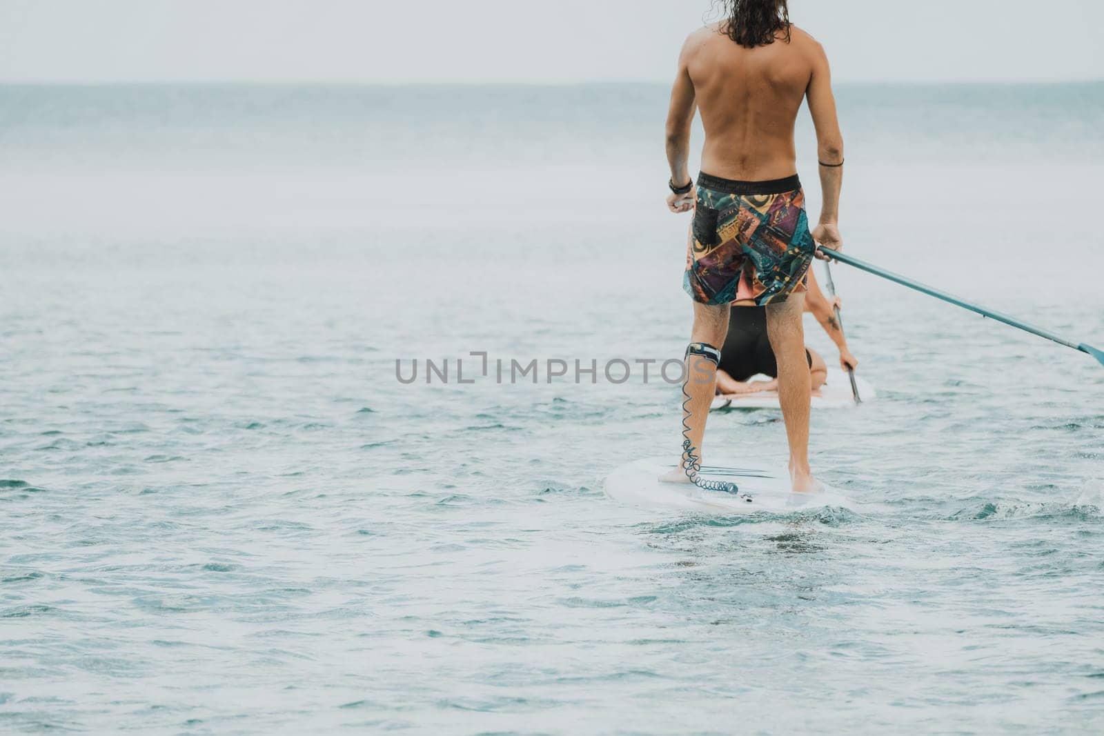 Sea woman and man on sup. Silhouette of happy young woman and man, surfing on SUP board, confident paddling through water surface. Idyllic sunset. Active lifestyle at sea or river